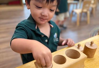 Toddler in a Montessori Kids Universe classroom working with knobbed cylinders
